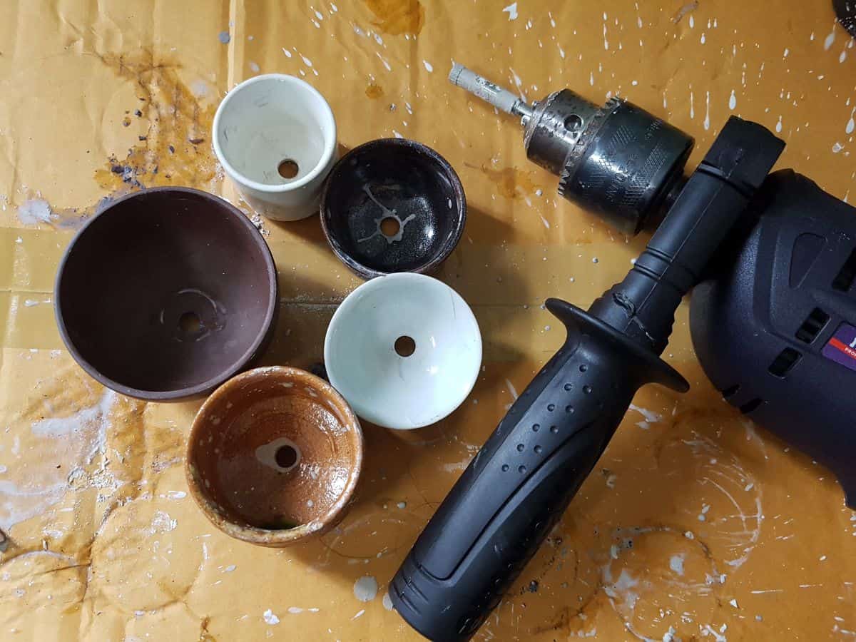 Pots with drilled hole and a driller on a table.