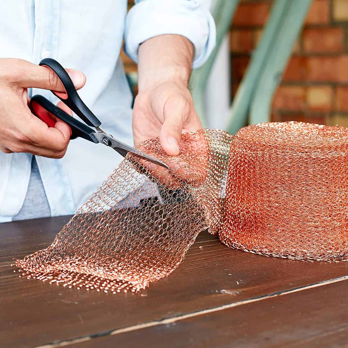 Hands cutting copper mesh with scissors.