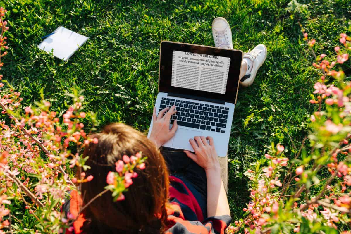 Girl with laptop sitting on the grass - gardening blog concept.