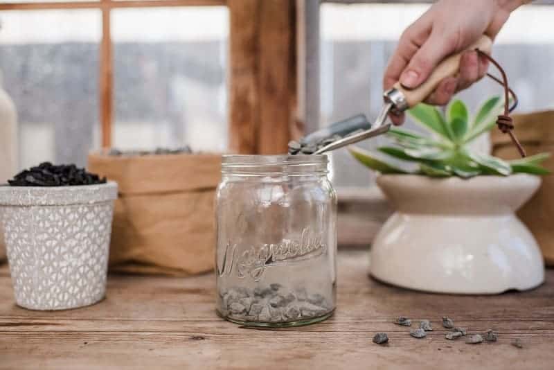 Hand with a gardening shovel pouring a soil into a glass pot.